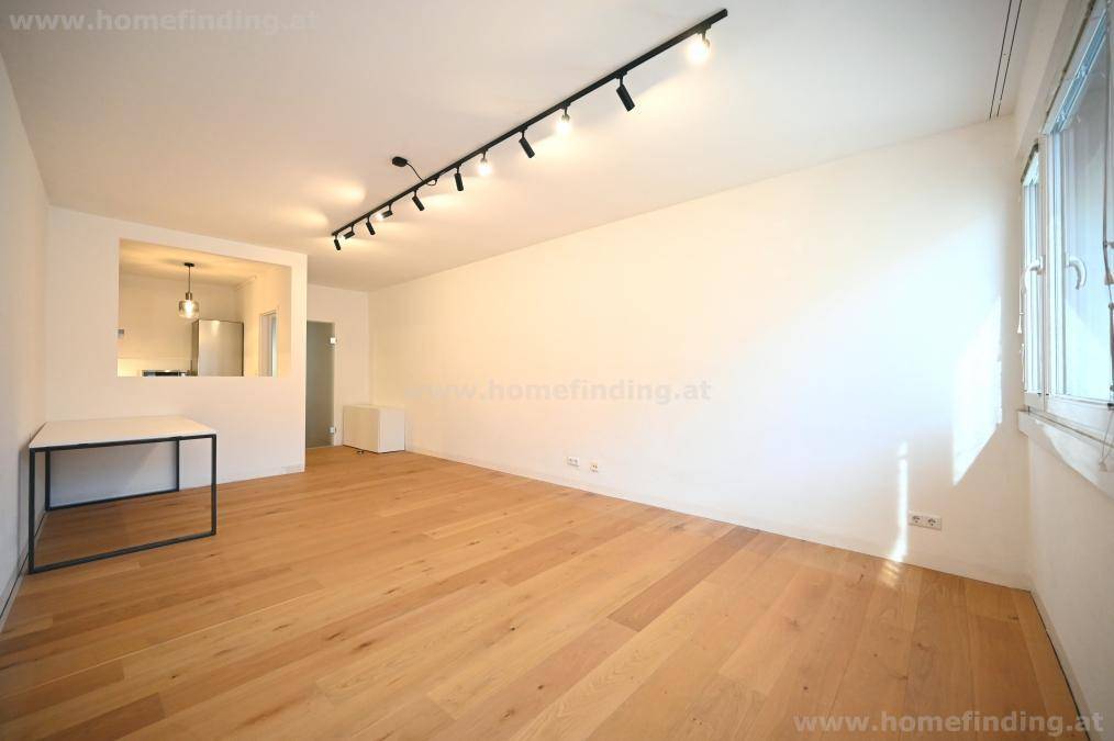 Geräumiges Wohnzimmer mit Holzboden und offenem Zugang zu einem Küchenbereich, ideal für modernes Wohnen.