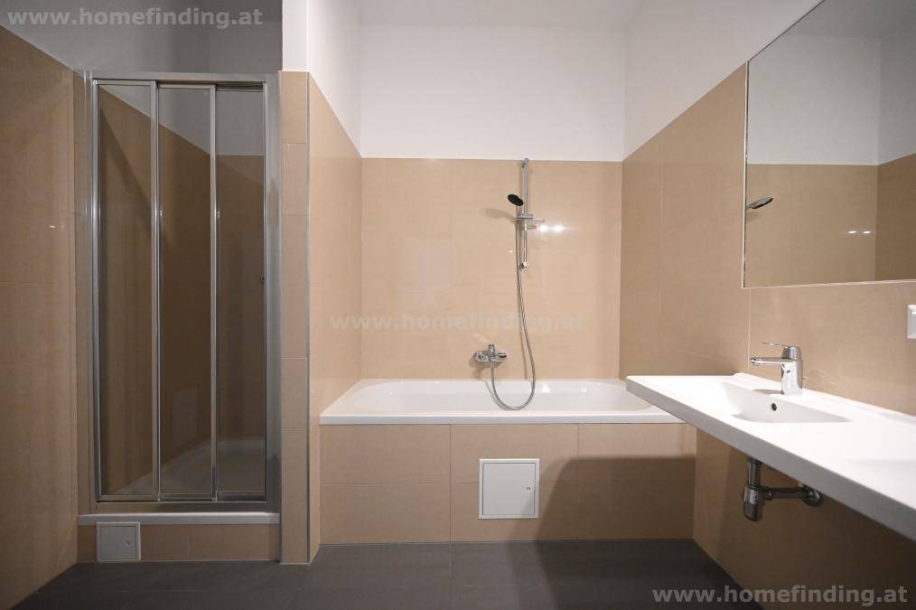 Helles Badezimmer mit beigefarbenen Fliesen, Badewanne mit Duschfunktion und Einzelwaschbecken.