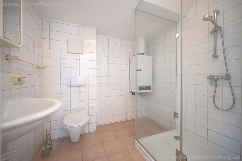 Badezimmer mit weißen Fliesen, Dusche, Waschbecken und Toilette.