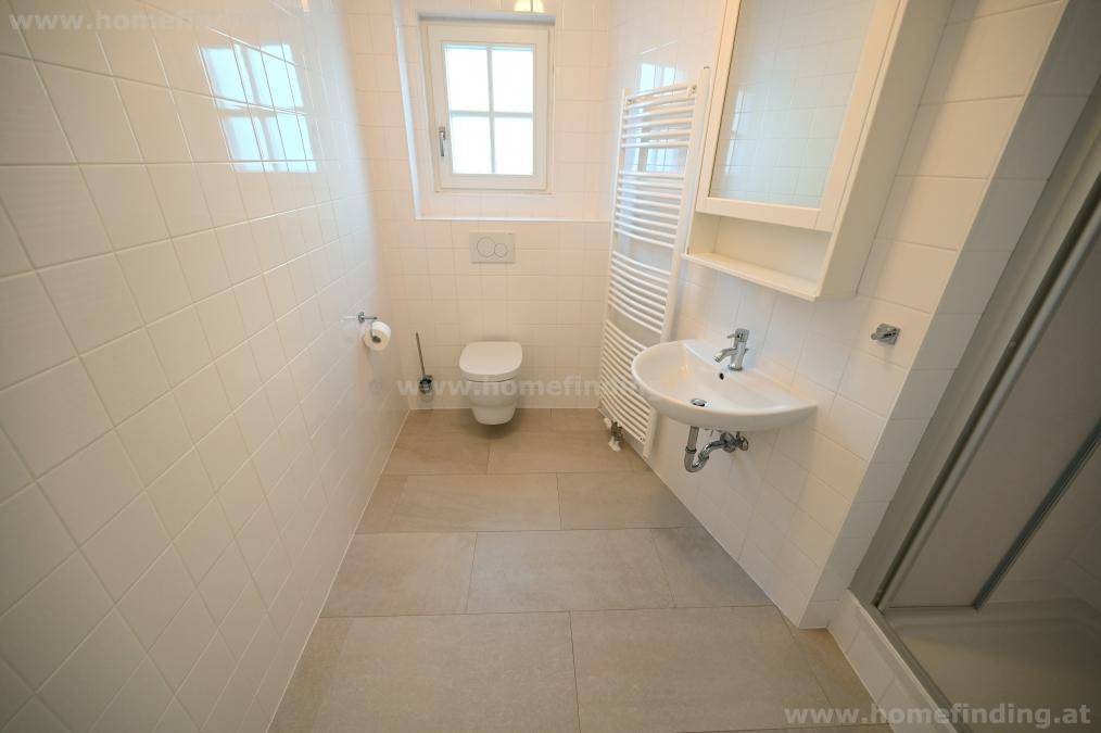 Helles Badezimmer mit Fenster, WC, Waschbecken, beheiztem Handtuchhalter und Spiegelschrank.