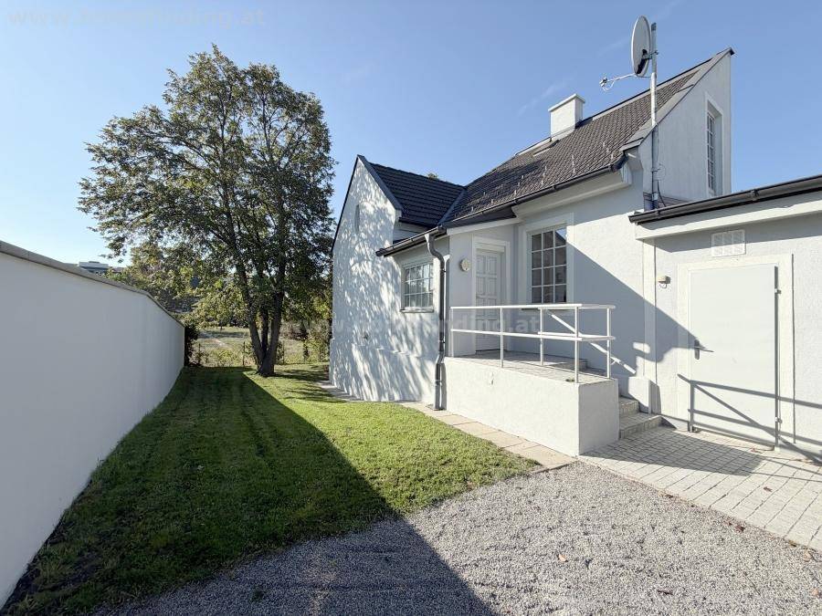 Außenansicht des Hauses mit gepflegtem Rasenbereich und Kiesweg unter blauem Himmel.