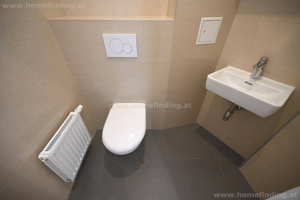 Separate Gästetoilette mit Wand-WC, kleinem Waschbecken und beigefarbenen Fliesen.
