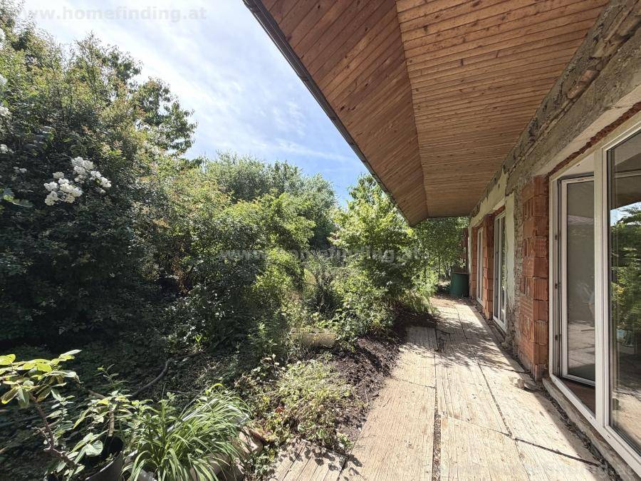Überdachte Terrasse mit Holzboden und üppiger grüner Vegetation im Garten.