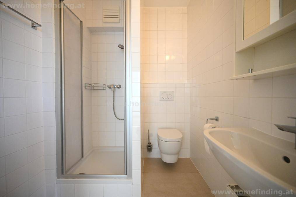 Funktionales Badezimmer mit Duschkabine, WC und Waschbecken, komplett weiß gefliest.