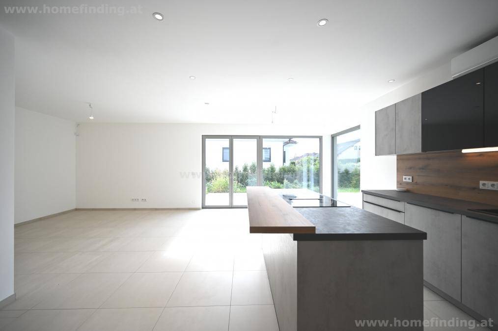 Geräumiger, offener Wohnbereich mit integrierter Küche, Fliesenboden und Zugang zur Terrasse.