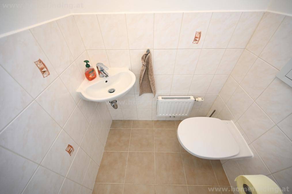 Kleines Gäste-WC mit Wand-WC, Handwaschbecken und hellen Fliesen an Wänden und Boden.
