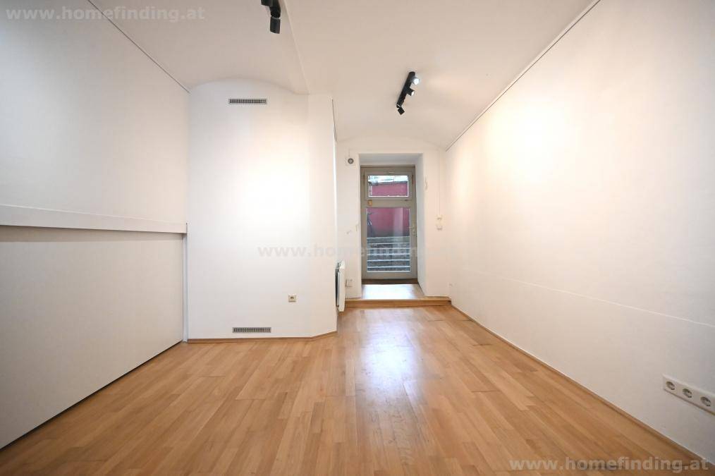 Lichtdurchfluteter Raum mit Holzboden, gewölbter Decke und Zugang zu einem kleinen Balkon.
