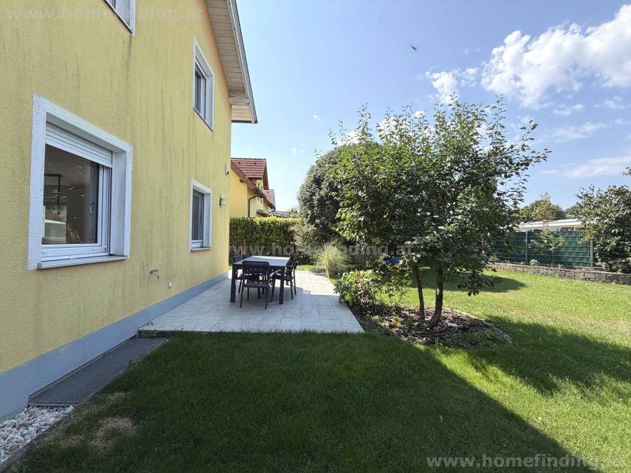 Sonniger Gartenbereich mit Terrasse, Rasenfläche und Sitzgelegenheiten neben dem Haus.