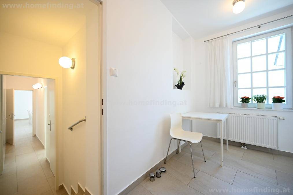 Heller Flur mit kleinem Tisch, Fenster und Blick in weitere Räume.