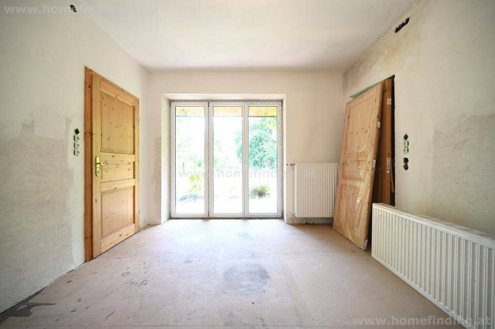 Unfertiger Raum mit Betonboden, Heizkörper und Holztür, bereit für die Renovierung.