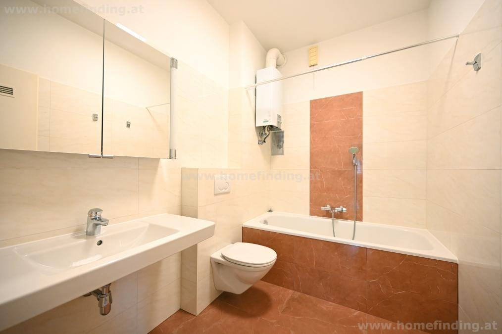 Badezimmer mit Badewanne, Waschbecken, WC und Spiegelschrank in hellen Fliesen.