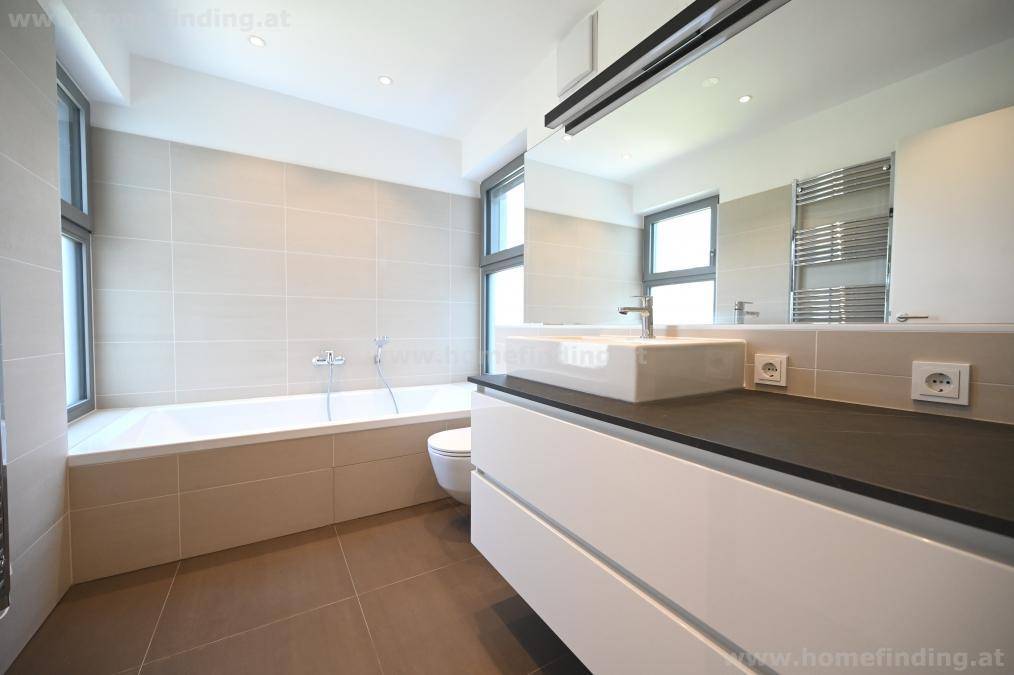 Modernes Badezimmer mit Badewanne, großem Waschtisch und hellen Fliesen, gut beleuchtet durch Fenster.