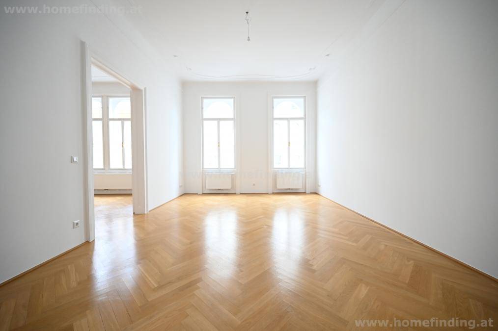 Geräumiges, helles Zimmer mit Fischgrätparkett und zwei hohen Fenstern, bereit zur Einrichtung.
