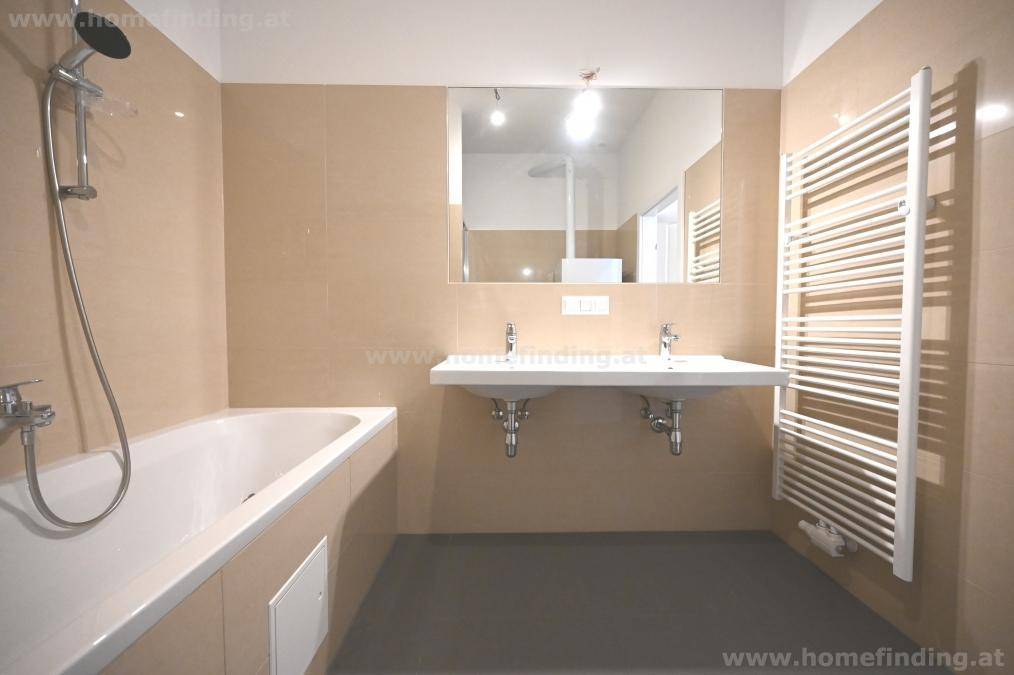 Helles Badezimmer mit Doppelwaschbecken, Badewanne und beheiztem Handtuchhalter.