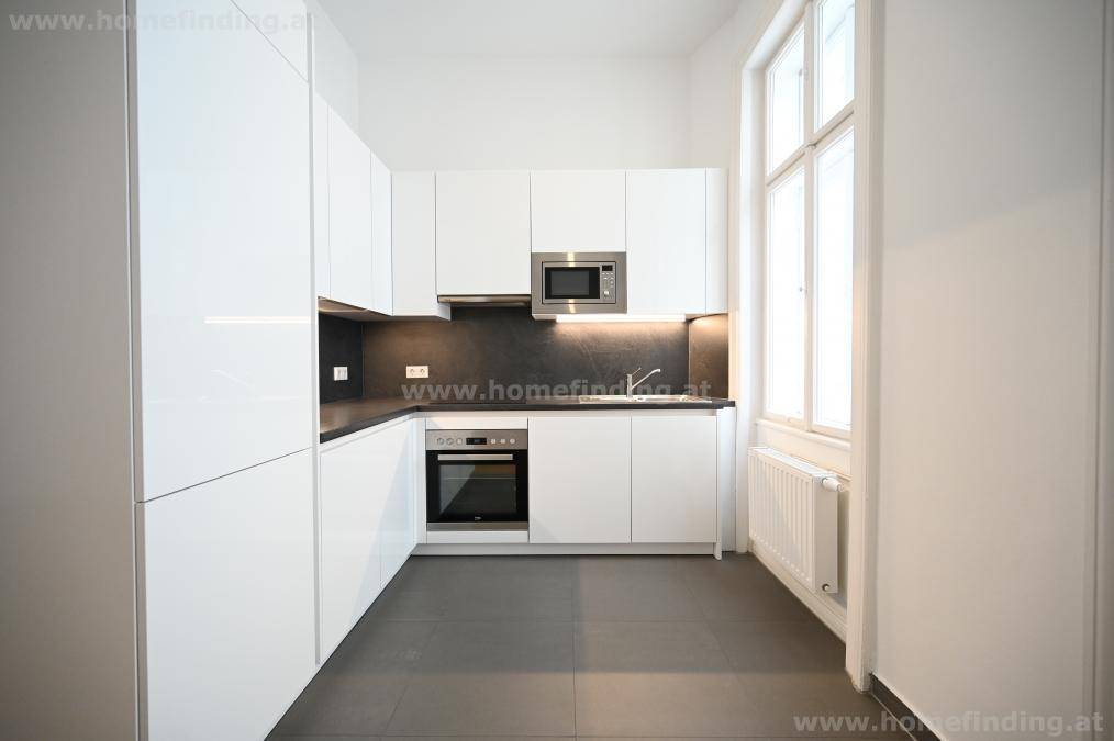 Moderne Einbauküche mit weißen Hochglanzfronten, dunkler Arbeitsplatte und Fenster.