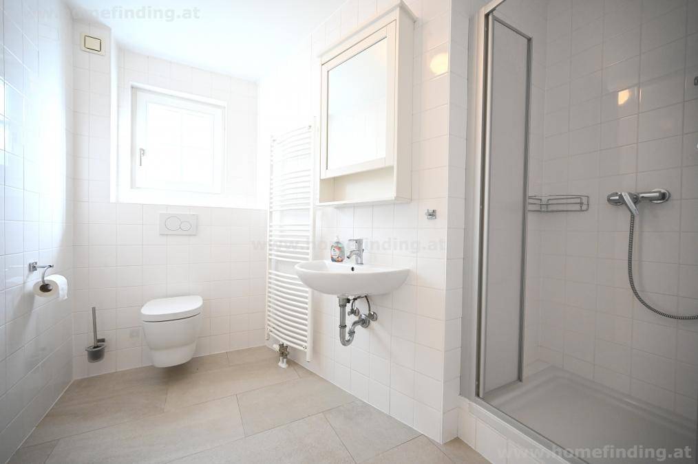Modernes Badezimmer mit Dusche, WC, Waschbecken, Fenster und weiß gefliesten Wänden.
