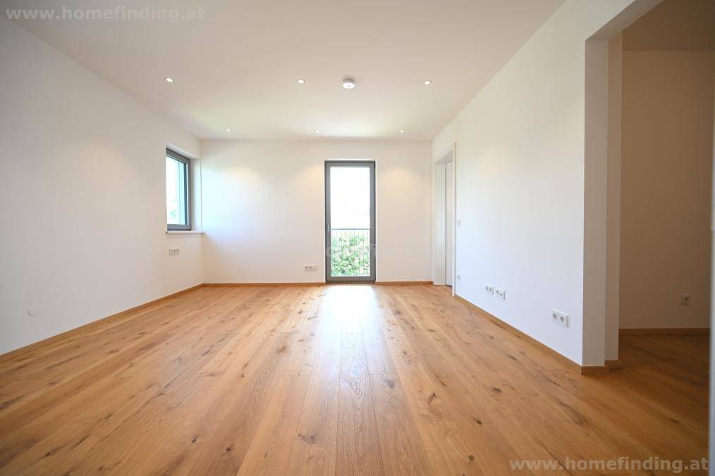 Leeres Zimmer mit hellem Holzparkett, großen Fenstern und Zugang zu einem französischen Balkon.