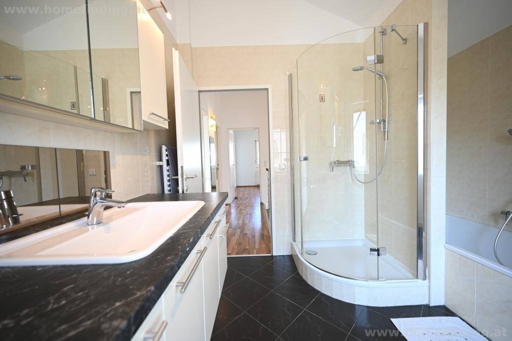 Badezimmer mit Waschtisch, Spiegelschränken, Duschkabine und Badewanne im Hintergrund.