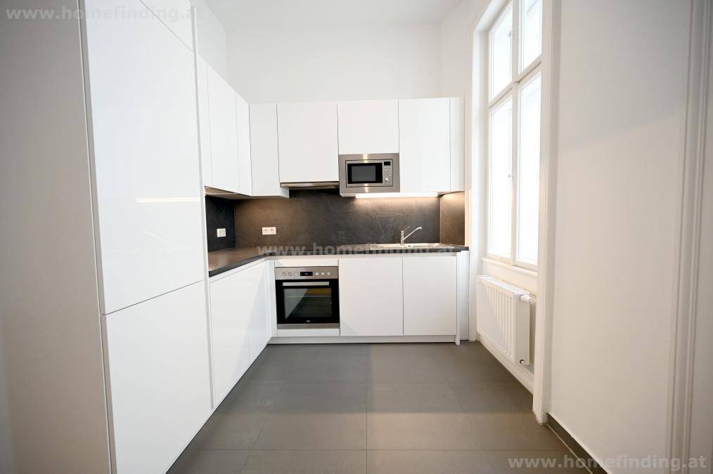 Kompakte, moderne Küche mit weißen Fronten, integrierten Geräten und Fenster.