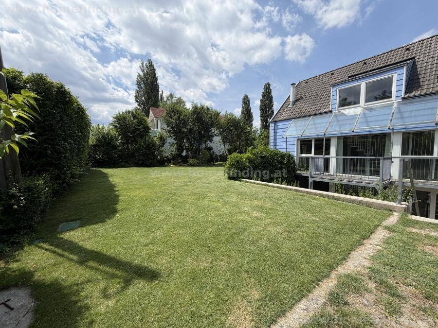Weitläufiger Garten mit gepflegtem Rasen und dem blauen Haus im Hintergrund unter blauem Himmel.