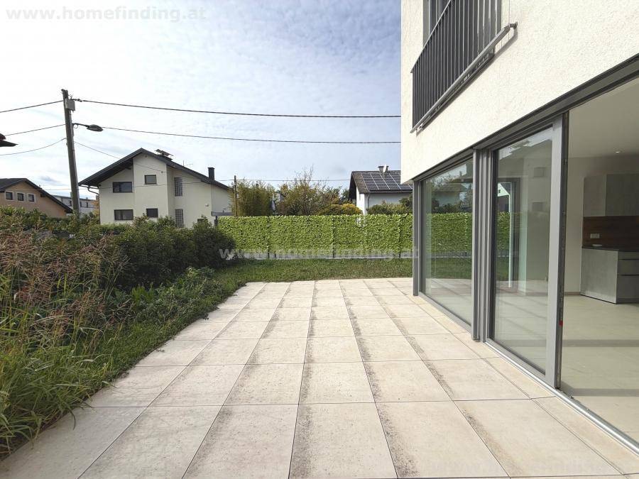 Große gepflasterte Terrasse neben dem Haus, umgeben von Grünflächen und einer Hecke.