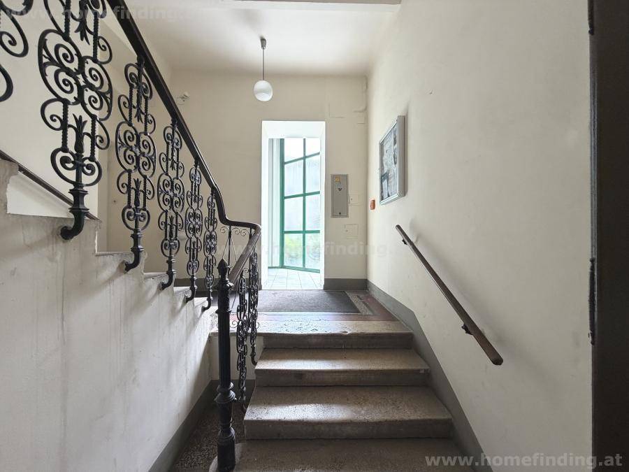 Historisches Treppenhaus mit schmiedeeisernem Geländer und Steinstufen, das den Charme des Altbaus unterstreicht.