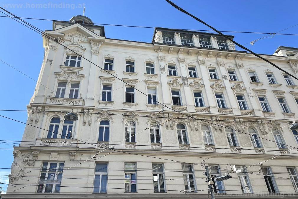Prächtige Altbaufassade mit vielen Fenstern und dekorativen Elementen unter blauem Himmel.