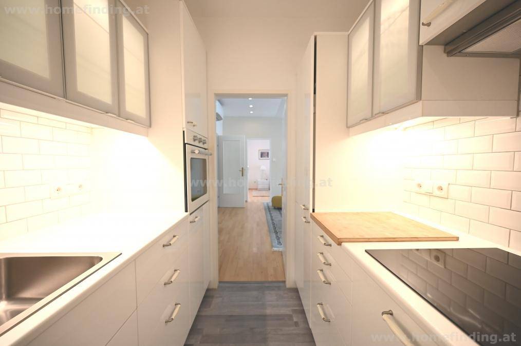 Moderne, schmale Küche mit weißen Schränken, Induktionskochfeld und integriertem Backofen.