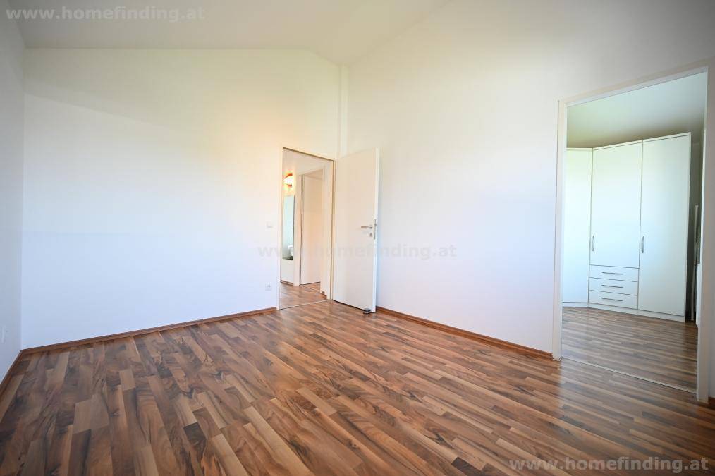 Helles Schlafzimmer mit Parkettboden und offenem Zugang zu einem Bereich mit Kleiderschrank.