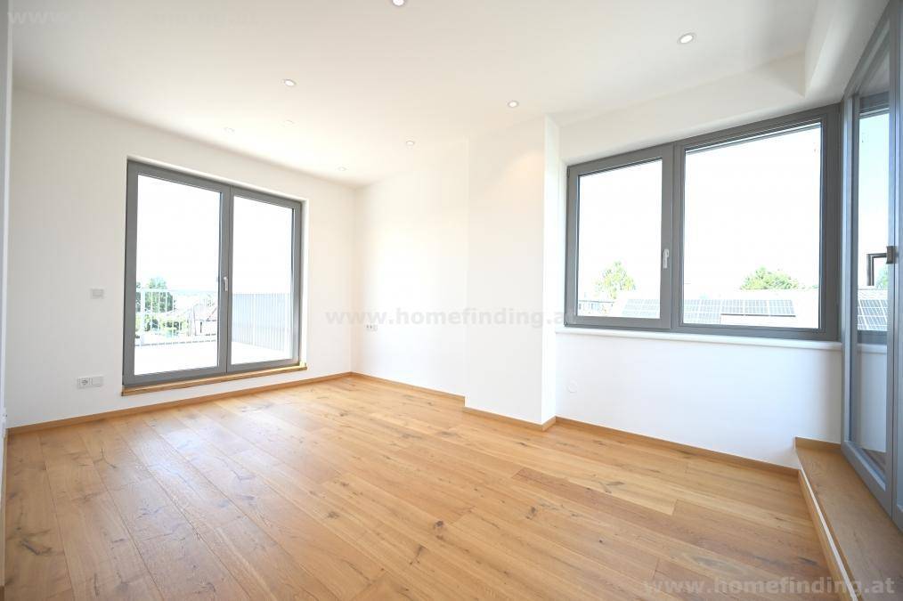 Helles Schlafzimmer mit Holzboden, großen Fenstern und Zugang zu einem Balkon oder einer Terrasse.