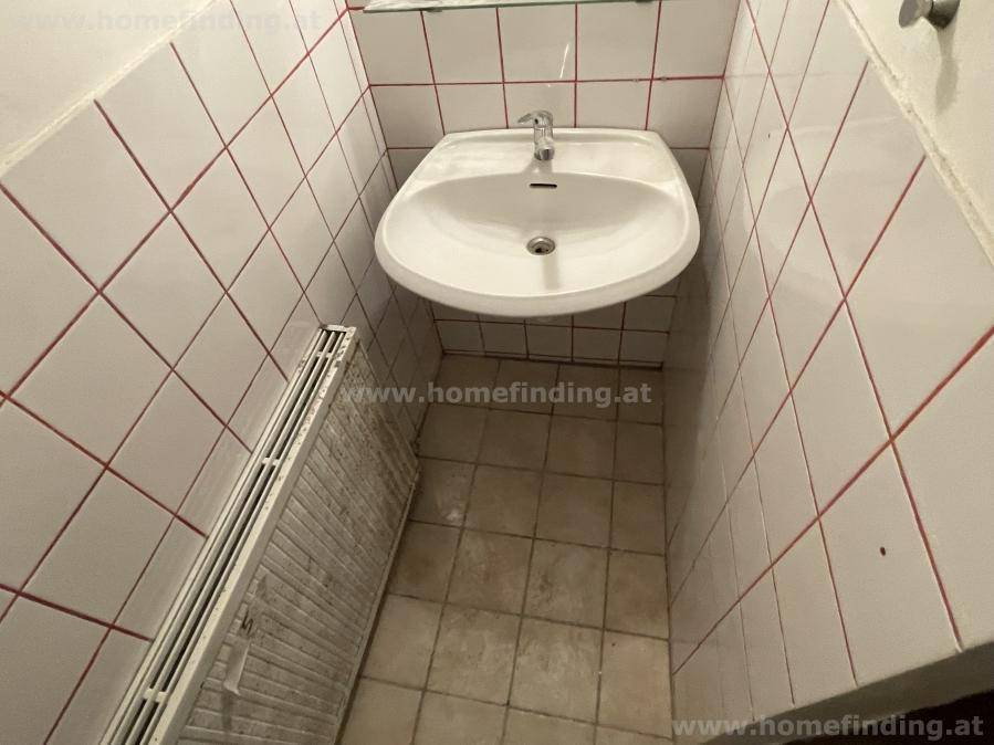 Kleiner Toilettenraum mit Waschbecken, Heizkörper und weiß-roten Wandfliesen, funktional eingerichtet.