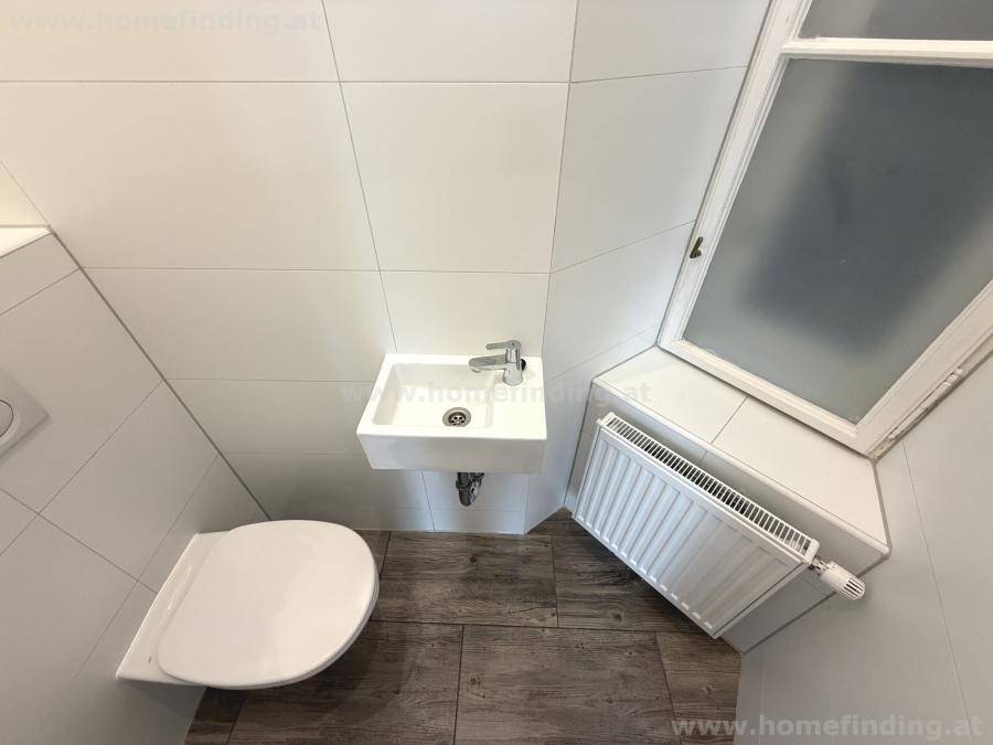 Modernes Gäste-WC mit wandhängender Toilette, kleinem Waschbecken und Fenster für Tageslicht.
