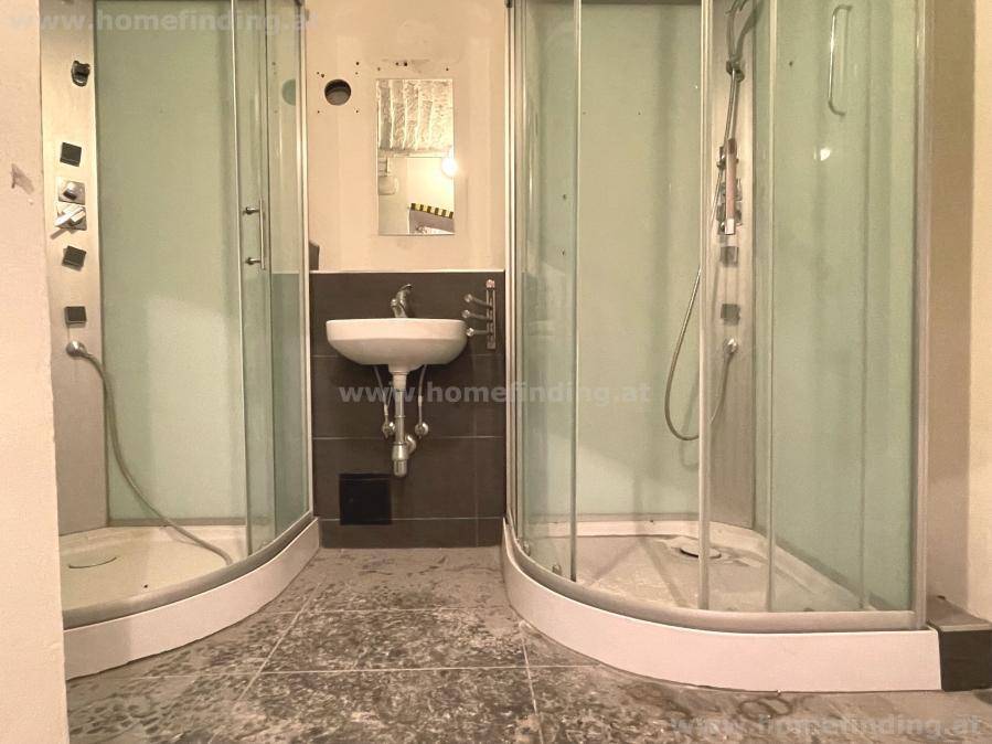 Badezimmer mit zwei Duschkabinen und einem Waschbecken, das eine Renovierung benötigt.