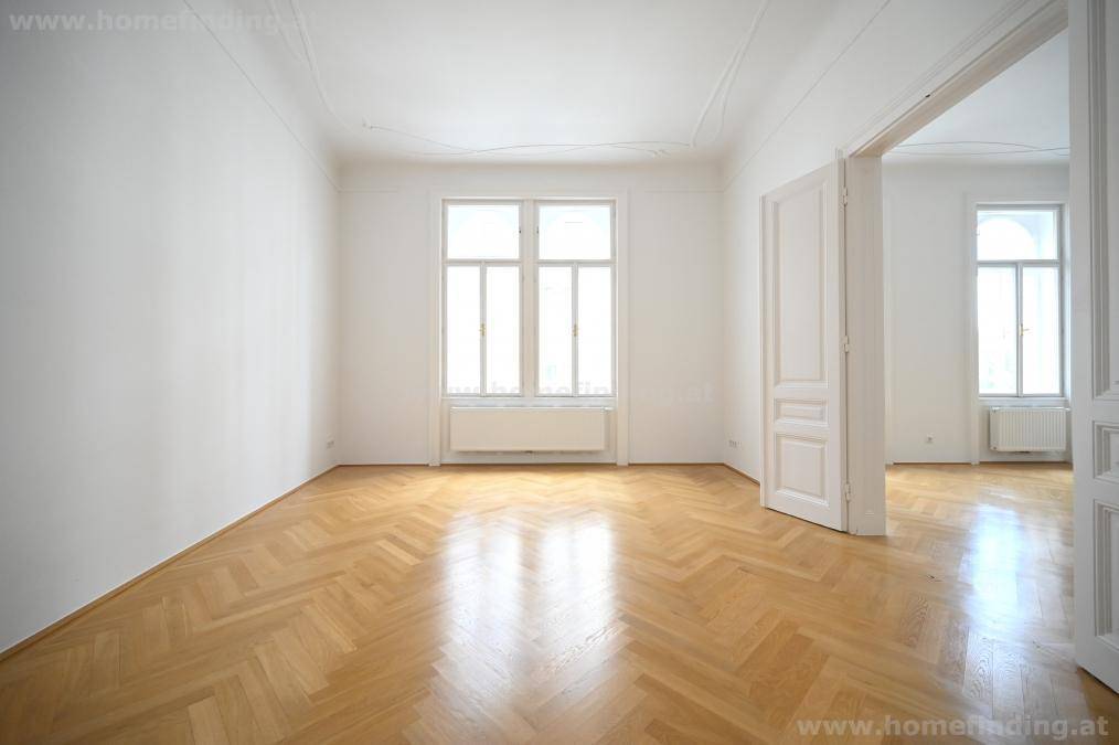 Großes, helles Zimmer mit Fischgrätparkett und hohen Fenstern, ideal als Wohnzimmer.