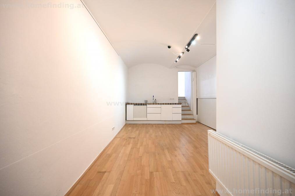 Heller Raum mit Holzboden, gewölbter Decke und einer integrierten Küchenzeile mit Spüle.