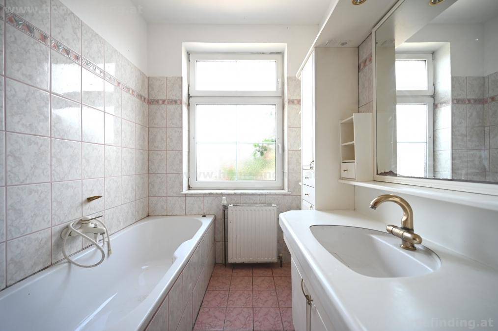 Badezimmer mit Badewanne, Waschbecken und Fenster, gefliest in hellen Tönen.