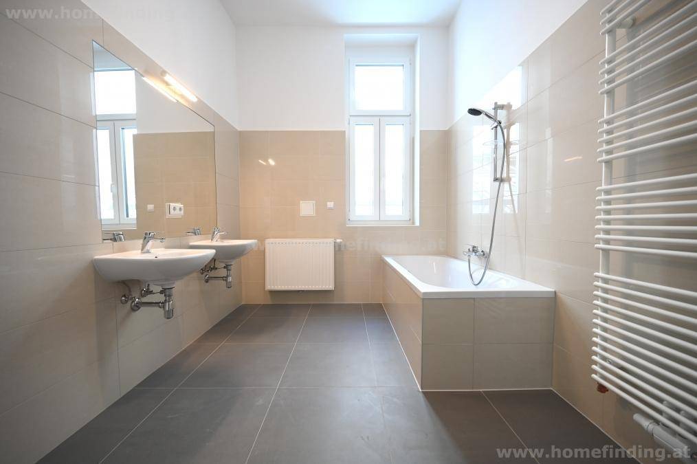 Modernes Badezimmer mit Doppelwaschbecken, Badewanne, Handtuchheizkörper und Fenster.