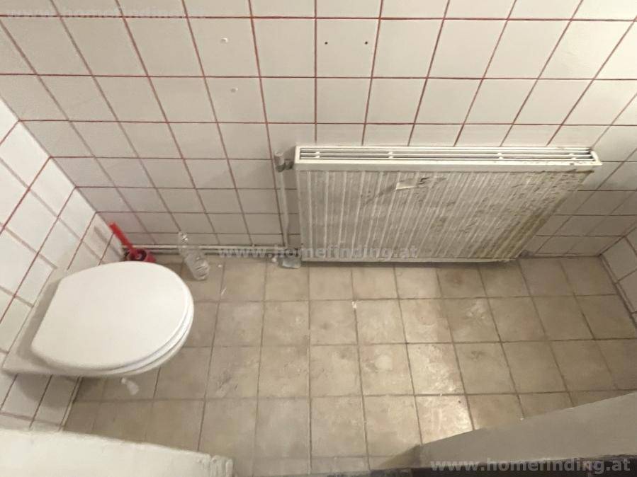 Kleiner Toilettenraum mit Fliesenboden, Heizkörper und weiß-roten Wandfliesen, einfach ausgestattet.