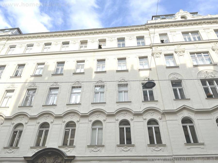 Klassische weiße Fassade eines Altbaus mit reich verzierten Details und vielen Fenstern.