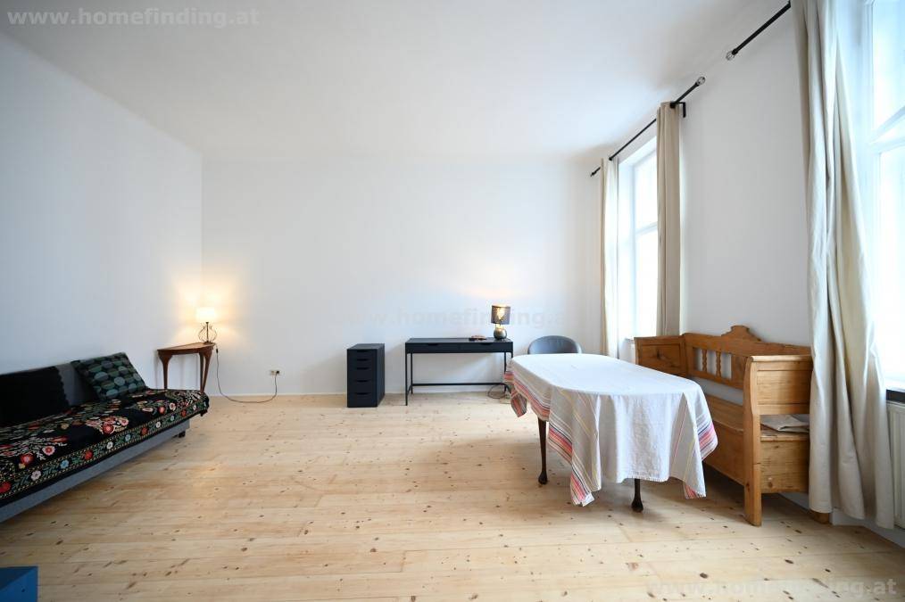Heller Wohnbereich mit Holzboden, Sofa, Esstisch und Schreibtisch, ideal für vielseitige Nutzung.
