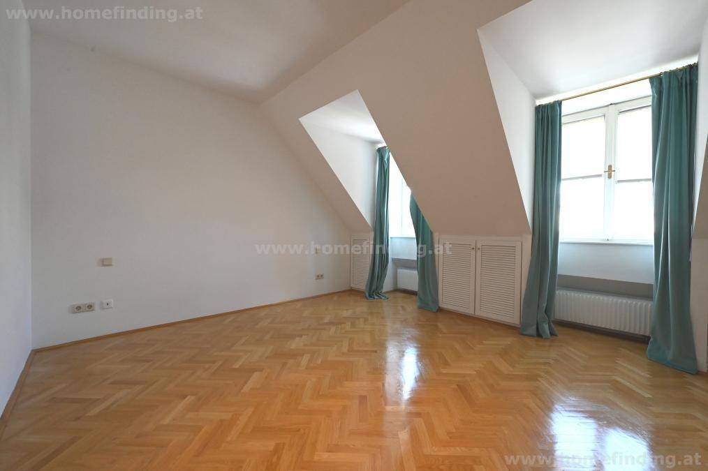 Schlafzimmer im Dachgeschoss mit schrägen Wänden, Parkettboden und hellen Vorhängen.