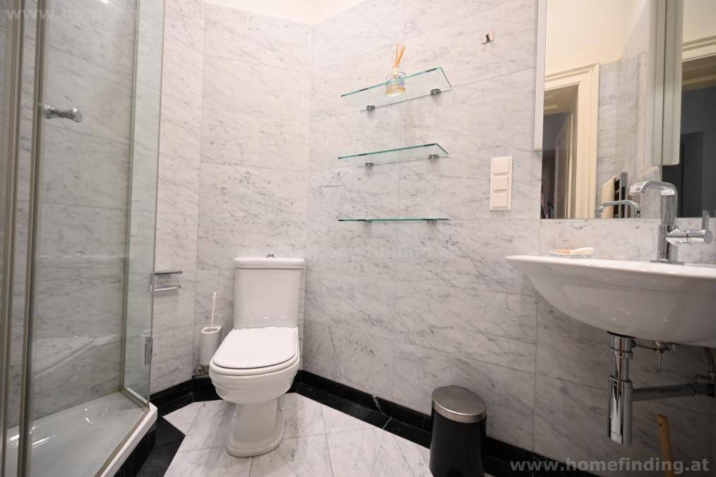 Elegantes Badezimmer mit Marmorfliesen, Duschkabine, Toilette und modernem Waschbecken für den täglichen Komfort.