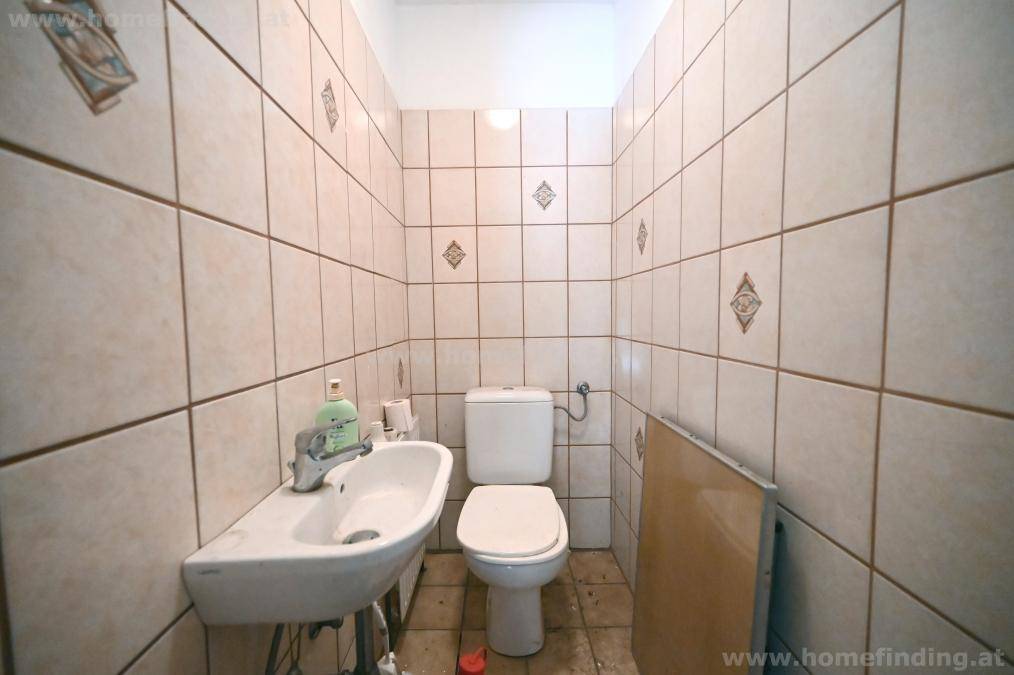 Separate Toilette mit Waschbecken und hellen Fliesen an den Wänden.