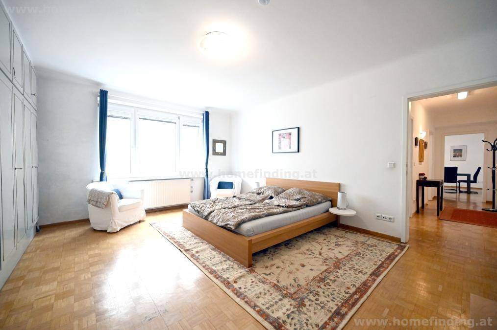 Gemütliches Schlafzimmer mit Holzbett, Parkettboden und großen Fenstern für viel Tageslicht.