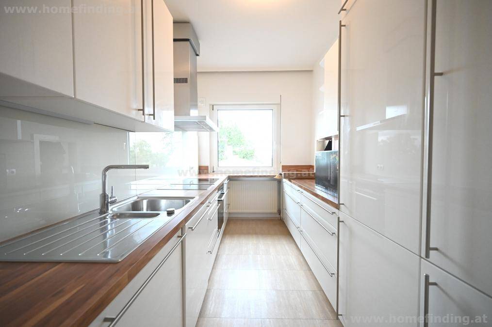 Moderne Küche mit weißen Hochglanzfronten, Holz-Arbeitsplatten und Fenster.