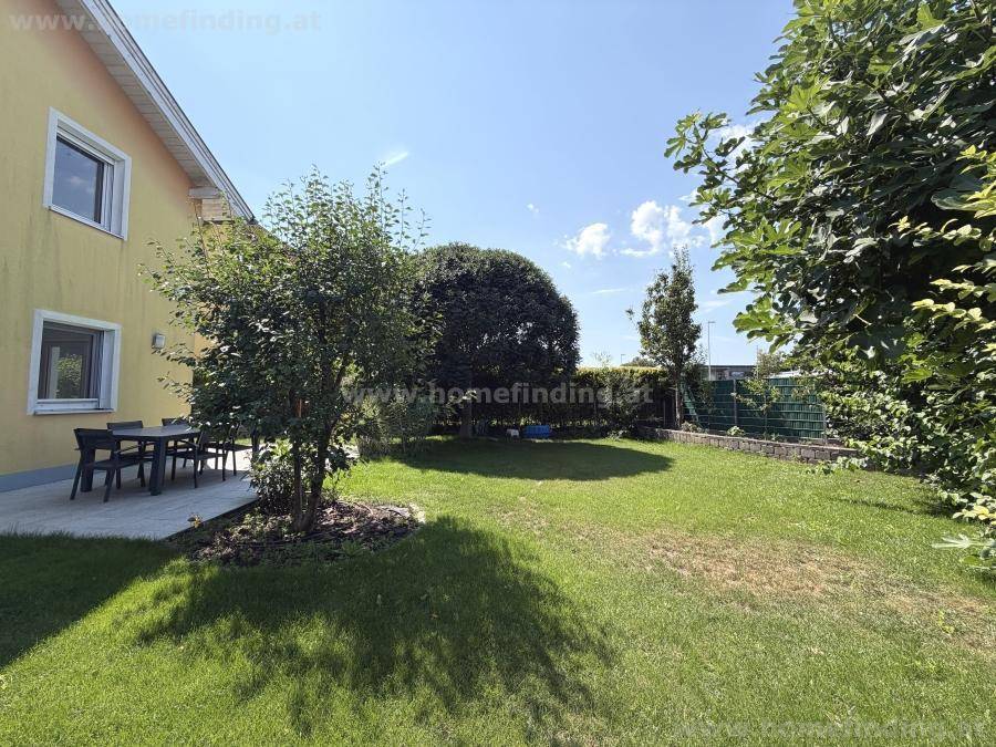 Großer, gepflegter Garten mit Rasenfläche, Bäumen und einer sonnigen Terrasse am Haus.