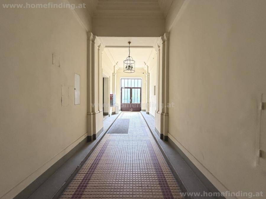 Langer, eleganter Eingangsbereich mit gemusterten Bodenfliesen und hohen Decken, der zum Gebäude führt.