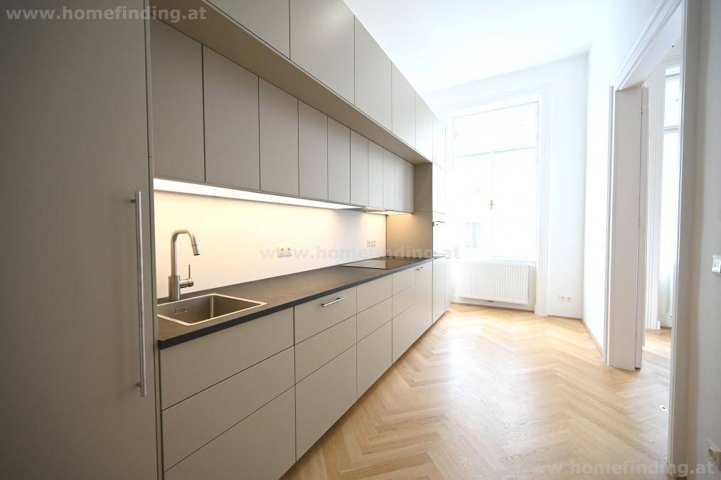 Helle, moderne Küche mit hellgrauen Schränken, Spüle und Induktionskochfeld, gut beleuchtet.