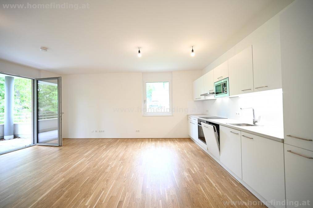 Heller offener Wohnbereich mit integrierter Küche, Parkettboden und Zugang zum Balkon.
