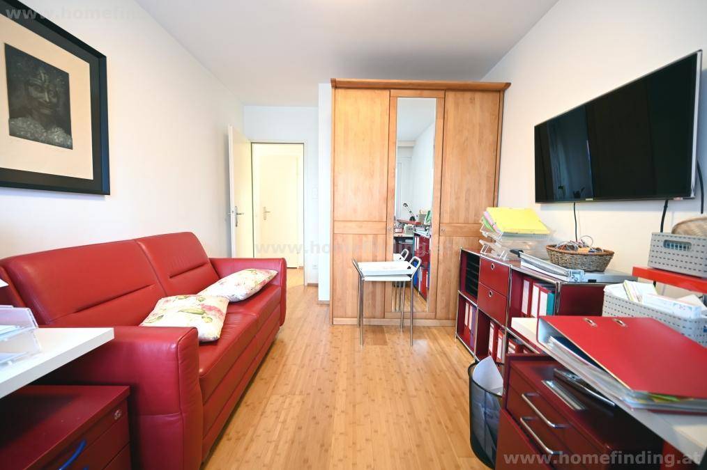 Arbeitszimmer oder Gästezimmer mit rotem Sofa, Holzschrank und Wandfernseher.